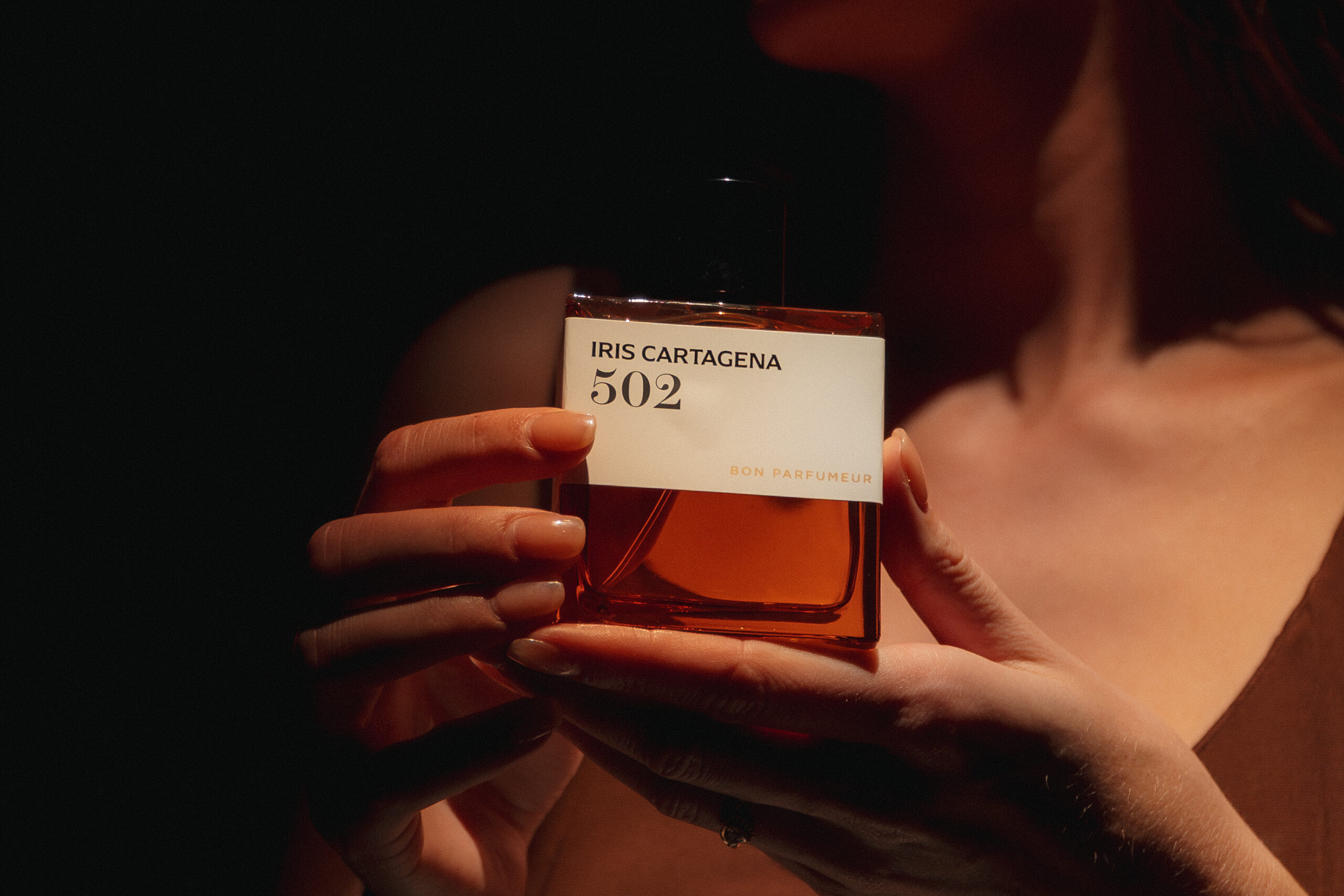 Jules Jessica holding Bon Parfumeur 502 Iris Cartagena amber bottle against skin in warm studio light, campaign production by 36 Studios